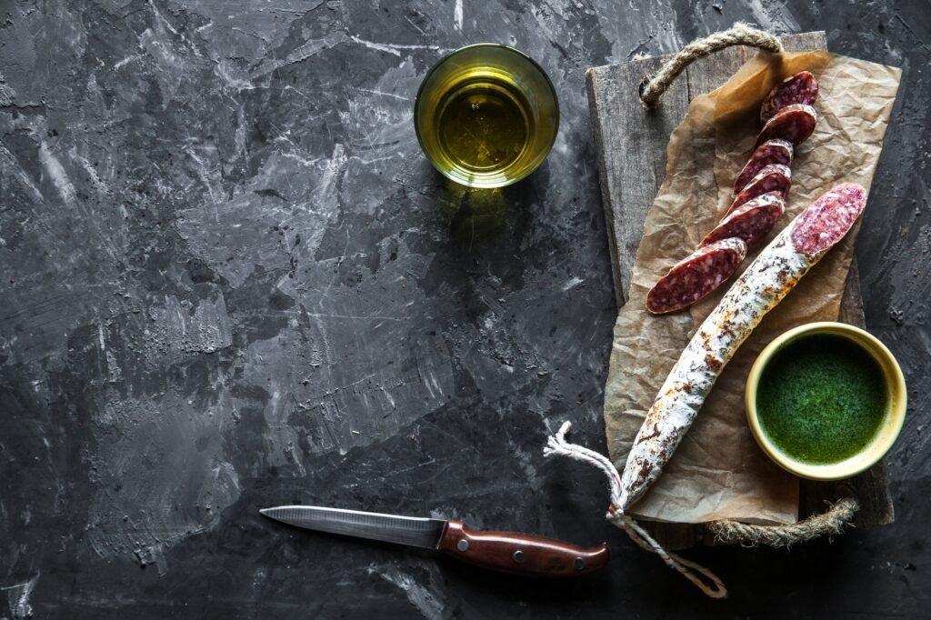 Sausage on a dark background with elements of cooking. Cucumber, onion, ketchup